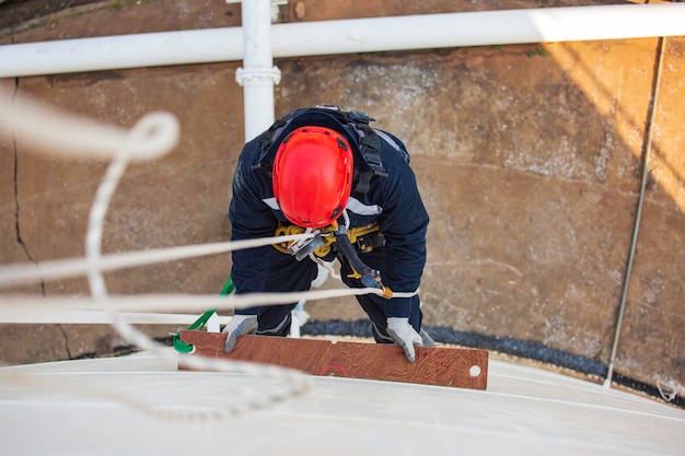 Top view pic of industrial rope access welder working at height wearing harness helmet safety equipment rope access inspection of thickness storage tank