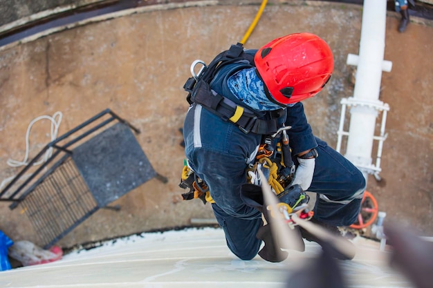 Top view pic of industrial rope access welder working at height\
wearing harness helmet safety equipment rope access inspection of\
thickness storage tank