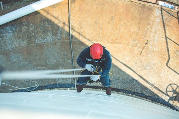 Top view pic of industrial rope access welder working at height wearing harness helmet safety equipment rope access inspection of thickness storage tank