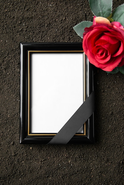 Top view of picture frame with red flower on a dark soil 