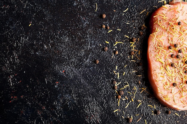 Vista dall'alto su un pezzo di carne cruda condita con pepe, sale e rosmarino secco su un tavolo di legno scuro