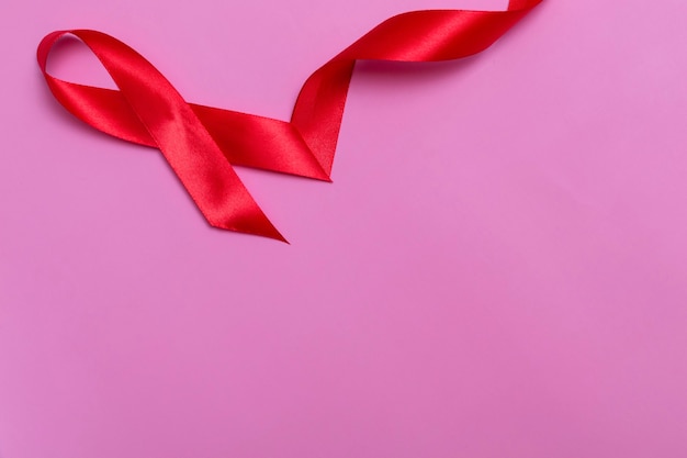 Top view on pink background with red ribbon concept December 1st International AIDS Day close-up.