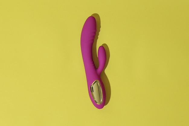 Top view of pink dildo vibrator on yellow background with shadows sex toy for adult
