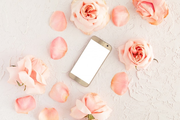 Top view of pink female desk with modern gold mobile phone with white blank screen and flowers