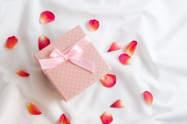 Vista dall'alto della confezione regalo rosa con petali di rosa su lenzuola bianche romantica sorpresa di san valentino e ...