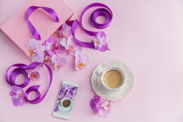 Top view of pink home office workspace with phone and coffee cup. Social media flat lay with coffee, flowers and smartphone. Female pink floral workplace