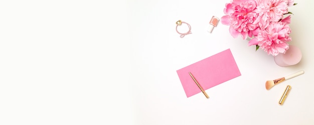 Vista dall'alto di una busta di carta rosa con una penna d'oro, accessori donna, un bouquet di peonie rosa, candele isolato su bianco