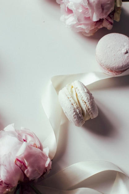 Top view of pink peonies and macaroons on a light background, a place for text