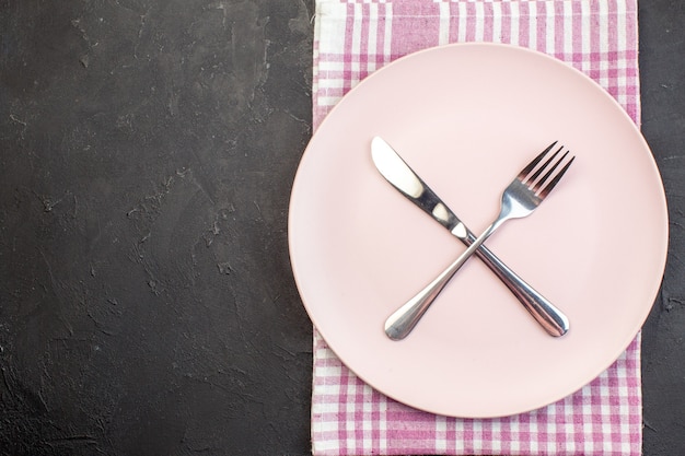 Top view pink plate with fork and knife on dark background