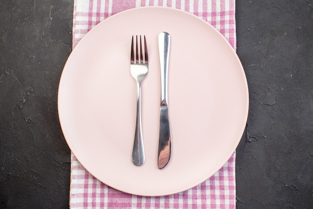 Top view pink plate with fork and knife on dark surface