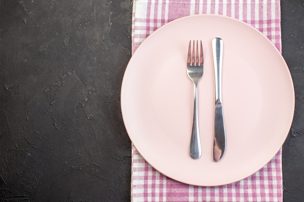 Top view pink plate with fork and knife on dark surface