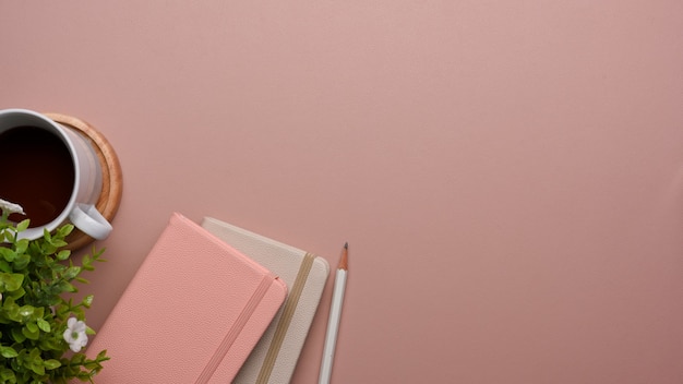 Vista dall'alto del tavolo rosa con libri di latticini, matita, vaso per piante, tazza di caffè e copia spazio, mock up scena