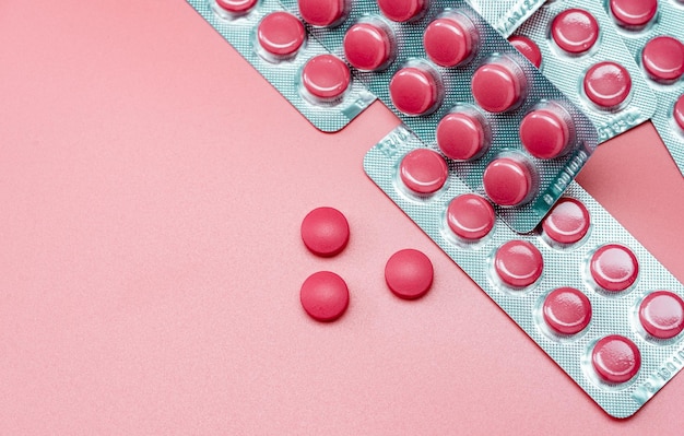 Top view of pink tablets pill and blister pack of pills on pink background Prescription drugs