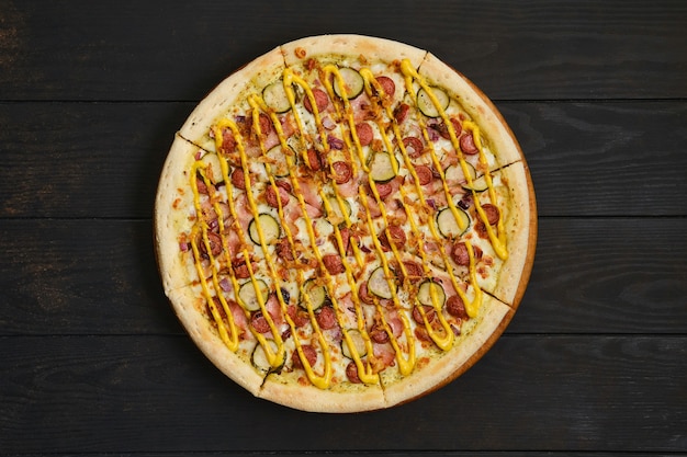 Вид сверху пиццы с колбасой, ветчиной, маринованным огурцом, луком и горчицей