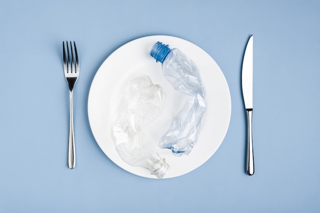 Foto vista dall'alto dei rifiuti di plastica nel piatto bianco, coltello e forchetta, salva l'ambiente dai problemi