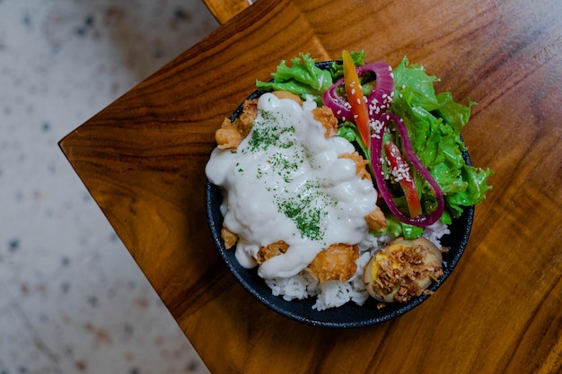 Photo top view of a plate of chicken rice with mayonnaise, vegetables and boiled egg in the wooden table