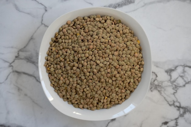 Top view of plate of raw lentils on marble tabletop