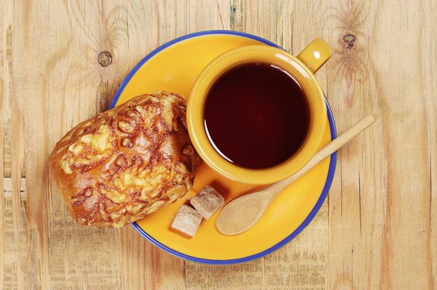 Top view on plate with fresh bun and cup of tea, located on the old wooden table