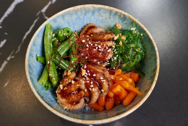 A top view of a poke bowl with octopuses Wakame seaweed carrot peanut sesame white rice on a black stone table