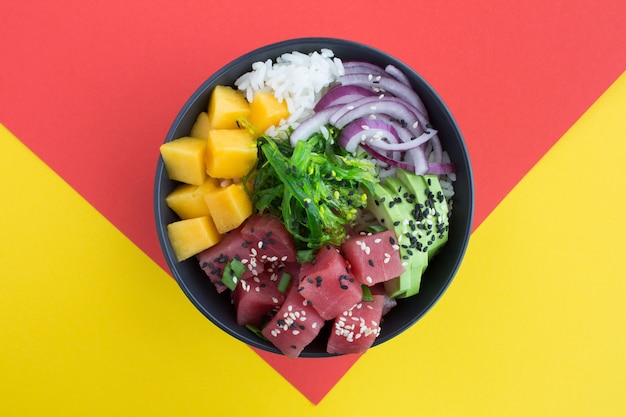 Top view of poke bowl with tuna in the dark bowl on the colorful surface