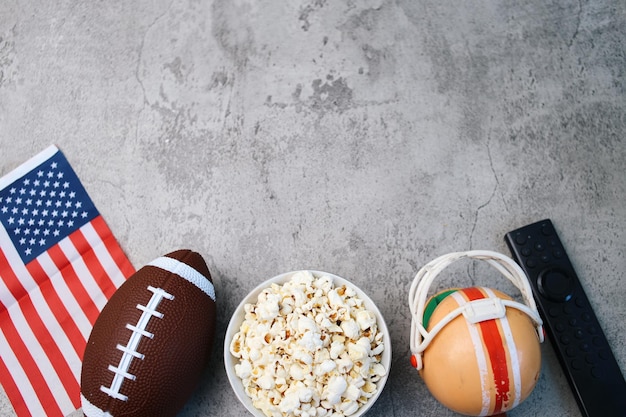 Foto vista superiore del popcorn palla da rugby con bandiera americana e telecomando su sfondo grigio con copia spa