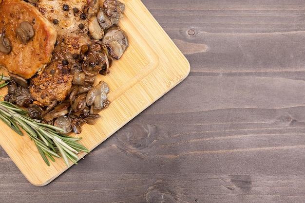 Over top view on pork steak with grilled mushrooms next to a brunch of oregano on wooden board