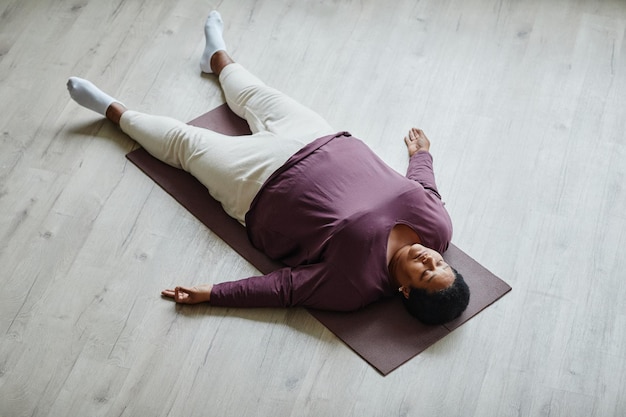 Top view portrait of black senior woman lying on floor with eyes closed while enjoying relaxation exercise