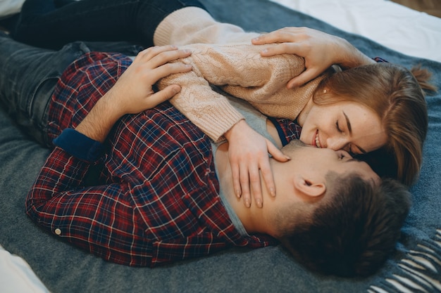 Top view portrait of a charming young couple embracing on a bed face to face laughing before kissing while girl is touching her boyfriends face .