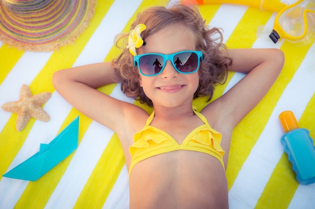 top view portrait of girl wearing blue sunglasses and laying down on striped beach towel