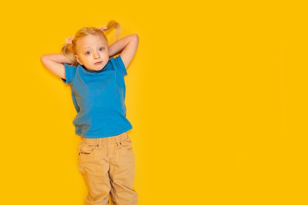 Top view portrait of preschool girl on bright yellow background Little girl in blue Tshirt lies with hands behind her head Copy space