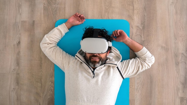 Top view portrait of tired caucasian fitness man resting after\
make exercise with a vr headset sportsman enjoying virtual reality\
glasses to practicing sport and lying on ground at living room\
house