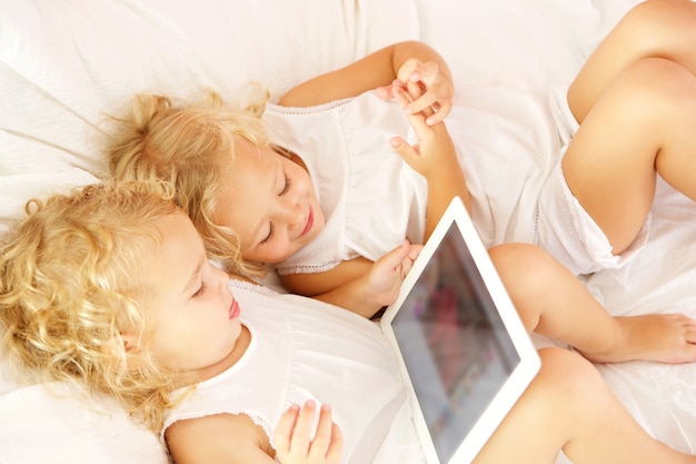 Top view portrait of two little sisters using digital tablet on bed