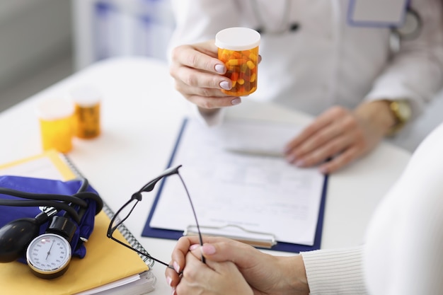 Top view of practitioner with bottle of capsules. Patient visiting doctor. Tonometer and documents on table. Medical prescription, treatment and healthcare concept