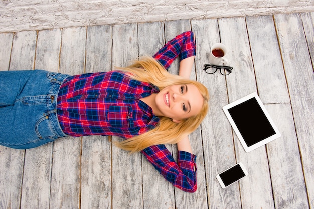 Top view of pretty blonde lying with tablet, phone, cup and glasses