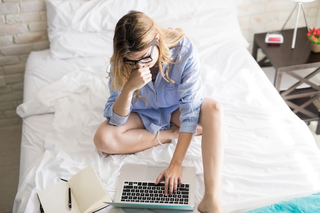 Top view of a pretty girl working and reading emails on her laptop computer while sitting on her bed at home