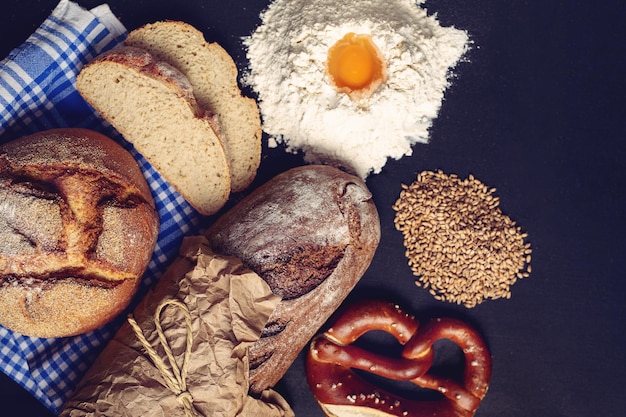 Top view of a pretzel, two loaves of bread, wheat and egg in flour