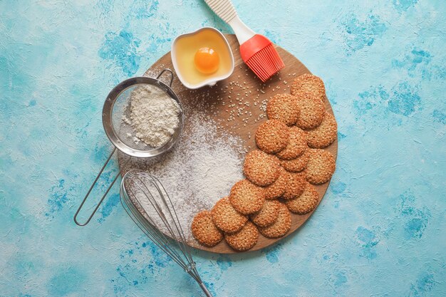 Top view of product set for cooking cookies, kitchenware and several round cookies with sesame on a blue wooden table