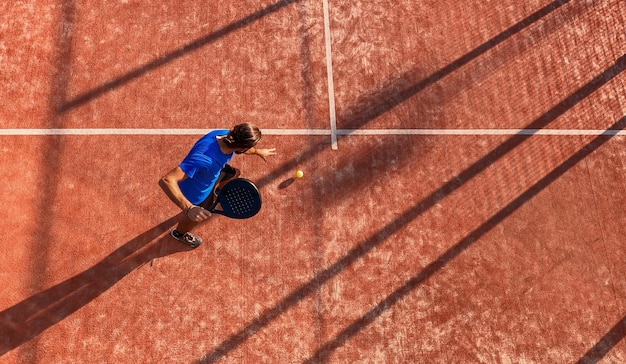 Top view of a professional paddle tennis player dribbling the ball on an outdoor court.