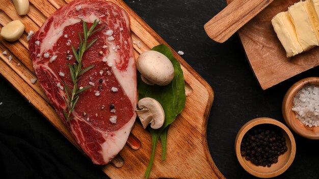 Top view Raw beef steak on top with rosemary and seasoning on a wooden board