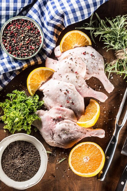 Top of view raw duck legs with oranges herbs rosemary cumin salt an pepper