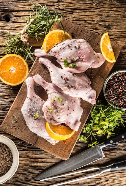 Top of view raw duck legs with oranges herbs rosemary cumin salt an pepper.