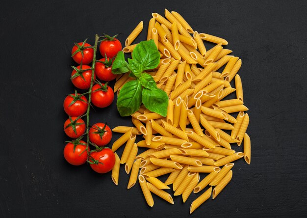 Top view of raw Italian pasta, tomatoes and basil