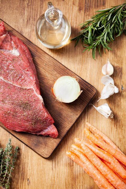 Top view of raw meat on cutting board seasoned with rosemary. Raw carreot. Virgin olive oil