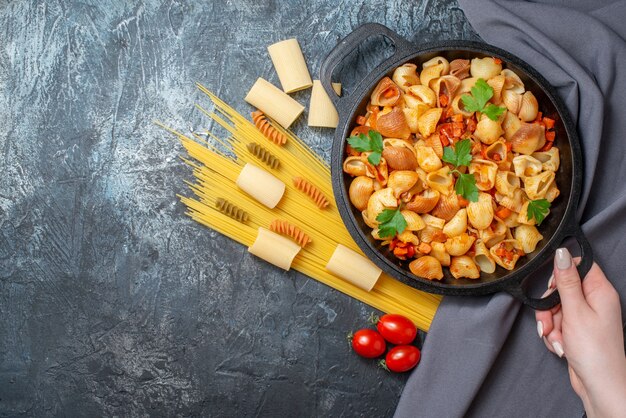 top view raw pastas spaghetti rigatoni spirals tasty pasta in frying pan in female hand on grey background copy place