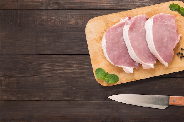 Photo top view raw pork chop steak on cutting board and knife on wooden background. copyspace for your text