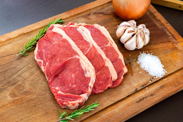 Top view of raw red meat sirloin steak with fat on a cutting board along with thyme garlic onion