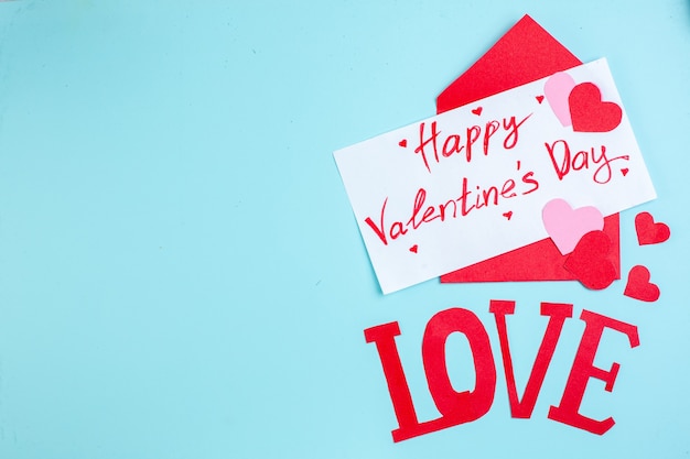 Photo top view red envelope happy valentines day written on letter red and pink hearts love capital letters on blue table copy place