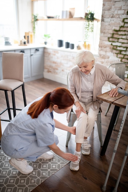 Top view of red-haired nurse lacing shoes for patient