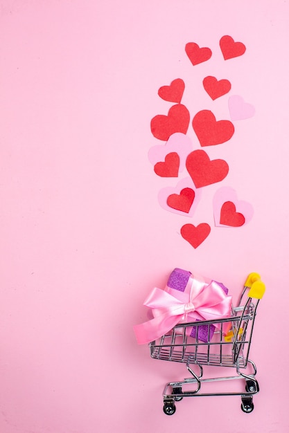 top view red heart stickers mini market trolley with gift on pink background free space