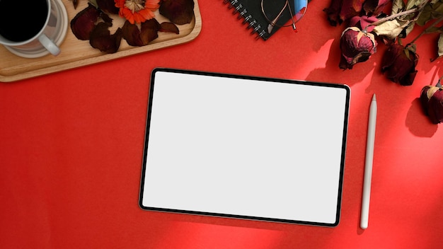 Top view of red office desk with digital tablet white screen mockup stylus pen and roses flower